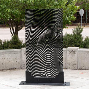 Metal sculpture sits on sidewalk in front of greenery