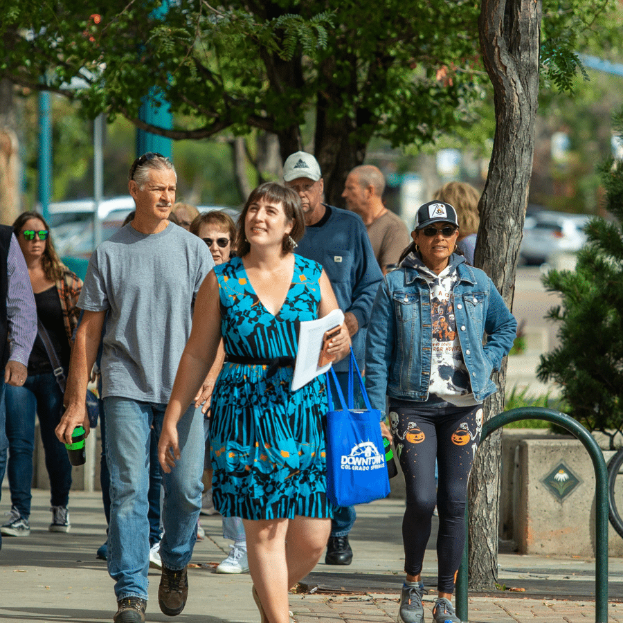 Woman leads walking tour group through park area with trees behind them