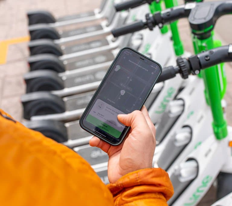 Person holding phone with Lime scooter app open in front of Lime scooters